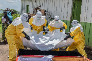 Red Cross workers carry the body of a person who died of Ebola into a coffin at a health center