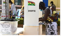A woman with a baby strapped to her back stands in a ballot box