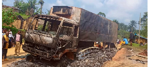 A charred wreckage of a truck stands on a road after it was burnt