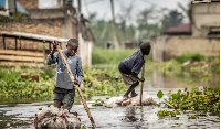 Children float on rafts made from plastic bottles on a flooded street in the Kinyinya III