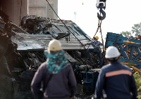Officials work at the site where a train was derailed when a construction crane collapsed