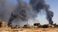 A man walks as smoke rises over buildings following air strikes during clashes between RSF  and army