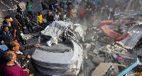 People gather near the remains of a car at the site of an Israeli strike on a house