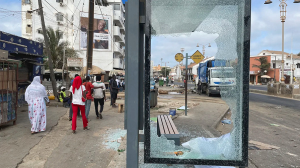 People walk past a bus shelter shattered during clashes between protesters and  security forces