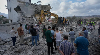 People watch rescue workers use an excavator as they conduct a search operation