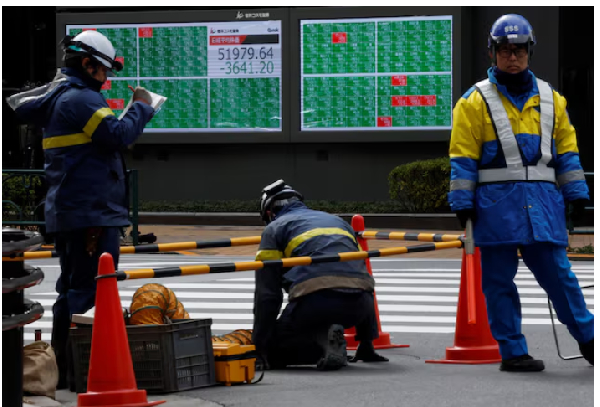 Workers carry out tasks near a stock quotation board showing the Nikkei share average outside a brok