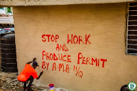 A man writing 'stop-work notice' on an incomplete building