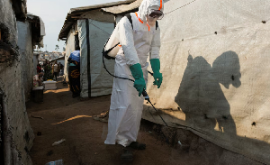A health worker in full personal protective equipment (PPE) is seen disinfecting an area
