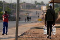 A man carrying water bottles walks along a dusty street in Hamanskraal, Pretoria