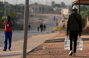 A man carrying water bottles walks along a dusty street in Hamanskraal, Pretoria A man carrying water bottles walks along a dusty street in Hamanskraal, Pretoria