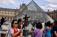 Tourists at the Louvre pose for pictures at the Paris Louvre Museum