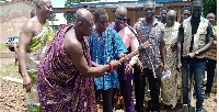 The minister (in smock) being assisted by Nana Kwabena Kyere III to cut the sod