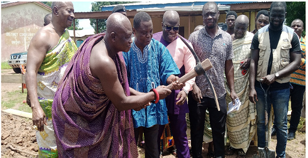 The minister (in smock) being assisted by Nana Kwabena Kyere III to cut the sod