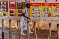 Health worker passes Ebola posters at Uganda-DRC border