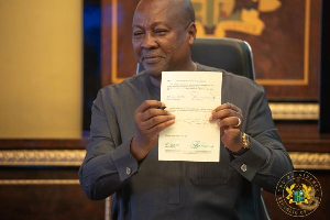 President John Dramani Mahama smiles as he shows the signed document to the public