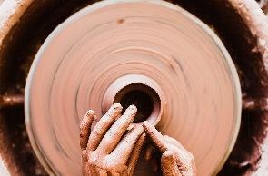 A person's hands crafting pottery on a spinning wheel. Original public domain image from Wikimedia