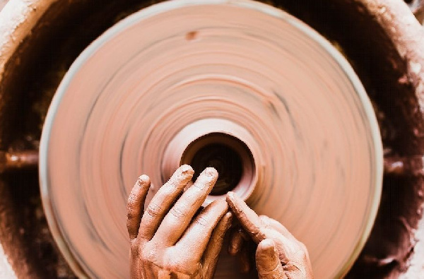 A person's hands crafting pottery on a spinning wheel. Original public domain image from Wikimedia