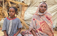 Zainab and her injured daughter sit outside their shelter in a displacement camp