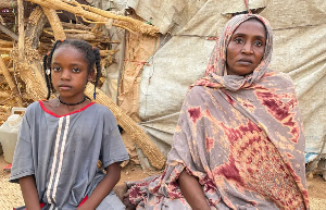 Zainab and her injured daughter sit outside their shelter in a displacement camp