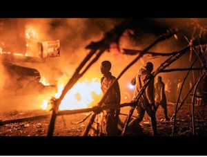 People walk by UN vehicles which were set on fire by angry crowds frustrated
