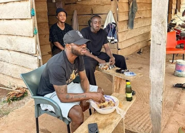 Ghana midfielder, Mubarak Wakaso (In a cap) enjoying food from wayside eatery