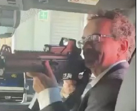 Screenshot from the video of Jon Benjamin pointing an assault rifle at his staff