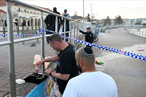 A man lights a candle as police officers stand guard the scene of the incident