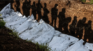 Residents cast their shadows as they observe members of the Congolese Red Cross conduct  mass burial