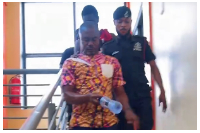 A police officer escorts the man allegedly linked to a UK visa fraud case from the Ahenfie FM studio