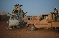 An Azawad Liberation Front (FLA) soldier stands on a pick-up truck next to a damaged helicopter