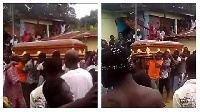 Undertakers carrying the deceased in a coffin with people gathered around the house