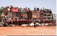 People sit atop a truck carrying household goods parked along the road connecting Khartoum