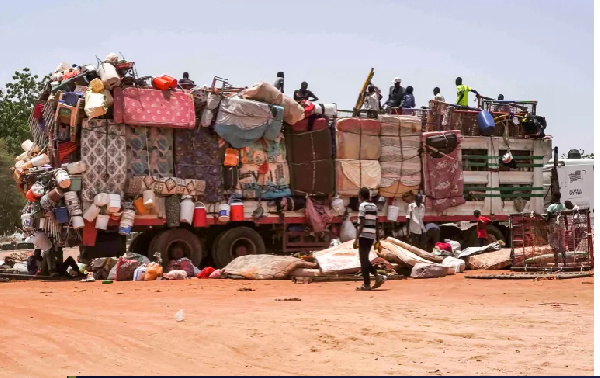 People sit atop a truck carrying household goods parked along the road connecting Khartoum
