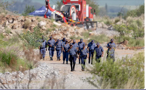 South African Police Service officers walk near the rescue operation to retrieve illegal miners