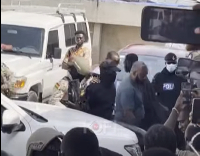 Abu Trica in all black flanked by heavy security