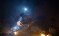 Lighted by a flashlight, a girl stokes the fire as the food is prepared in Bansang, Gambia