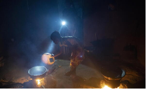 Lighted by a flashlight, a girl stokes the fire as the food is prepared in Bansang, Gambia
