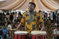 A photo of a young vibrant man playing traditional drums to communicate to the crowd