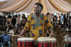 A photo of a young vibrant man playing traditional drums to communicate to the crowd