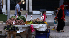 People walk next to a cart with prices of vegetables on a street in the port city of Alexandria, Egy