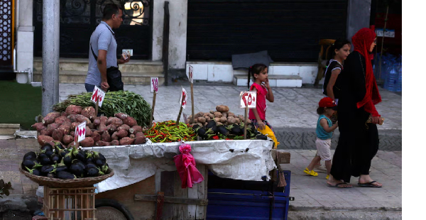 People walk next to a cart with prices of vegetables on a street in the port city of Alexandria, Egy