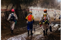 Miners wearing safety equipment walk through an underground tunnel at the South Deep gold mine