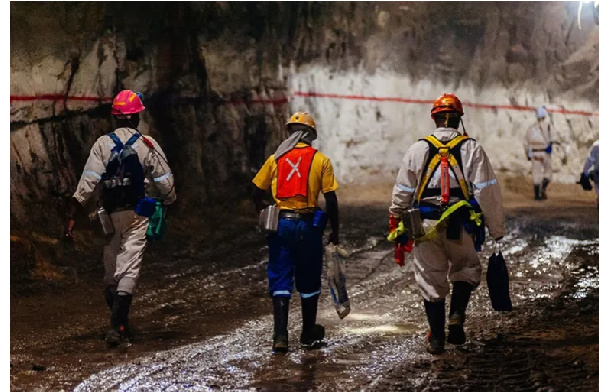 Miners wearing safety equipment walk through an underground tunnel at the South Deep gold mine