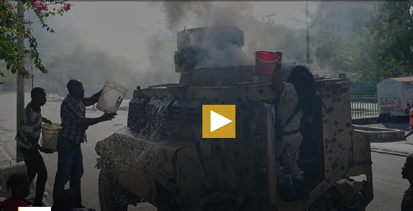 Police and civilians attempt to put out a fire set by gang members on an armored police vehicle