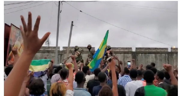 A military vehicle passes by people celebrating in Gabon after military officers announced coup