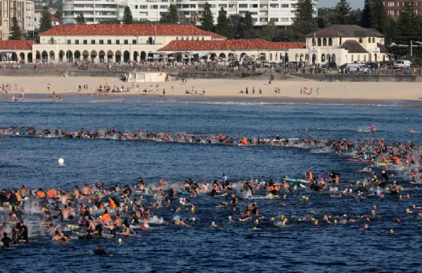 Surfers and swimmers congregate in the surf at Bondi Beach as they participate in a tribute