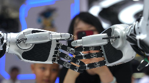 A woman and child watch a robot thread a needle at the World Robot Conference in Beijing