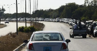 Libyan men walk past a long queue of cars waiting for fuel in Tripoli