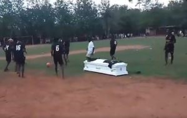 Casket of the deceased (white) on the pitch as football match is ongoing