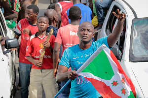 A demonstrator holds the Burundi national flag and makes the victory sign as he and others celebrate A demonstrator holds the Burundi national flag and makes the victory sign as he and others celebrate